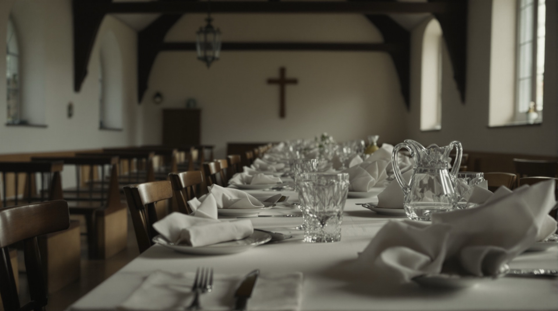 A long table set for a church supper with plain white crockery and folded paper napkins in an empty hall